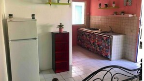 Una cuina compacta amb nevera, una prestatgeria vermella i un frontissis ple de color.