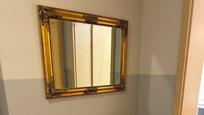 Un tocador de madera con espejo de marco dorado, dos cestas de mimbre y un florero de vidrio con una flor roja.