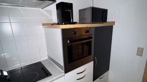 Una cocina compacta con estufa, horno, microondas y cafetera integrados en un estante.