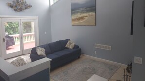 Ein Wohnzimmer mit blauem Sofa, einem Strandbild und Blick durch eine Glastür.