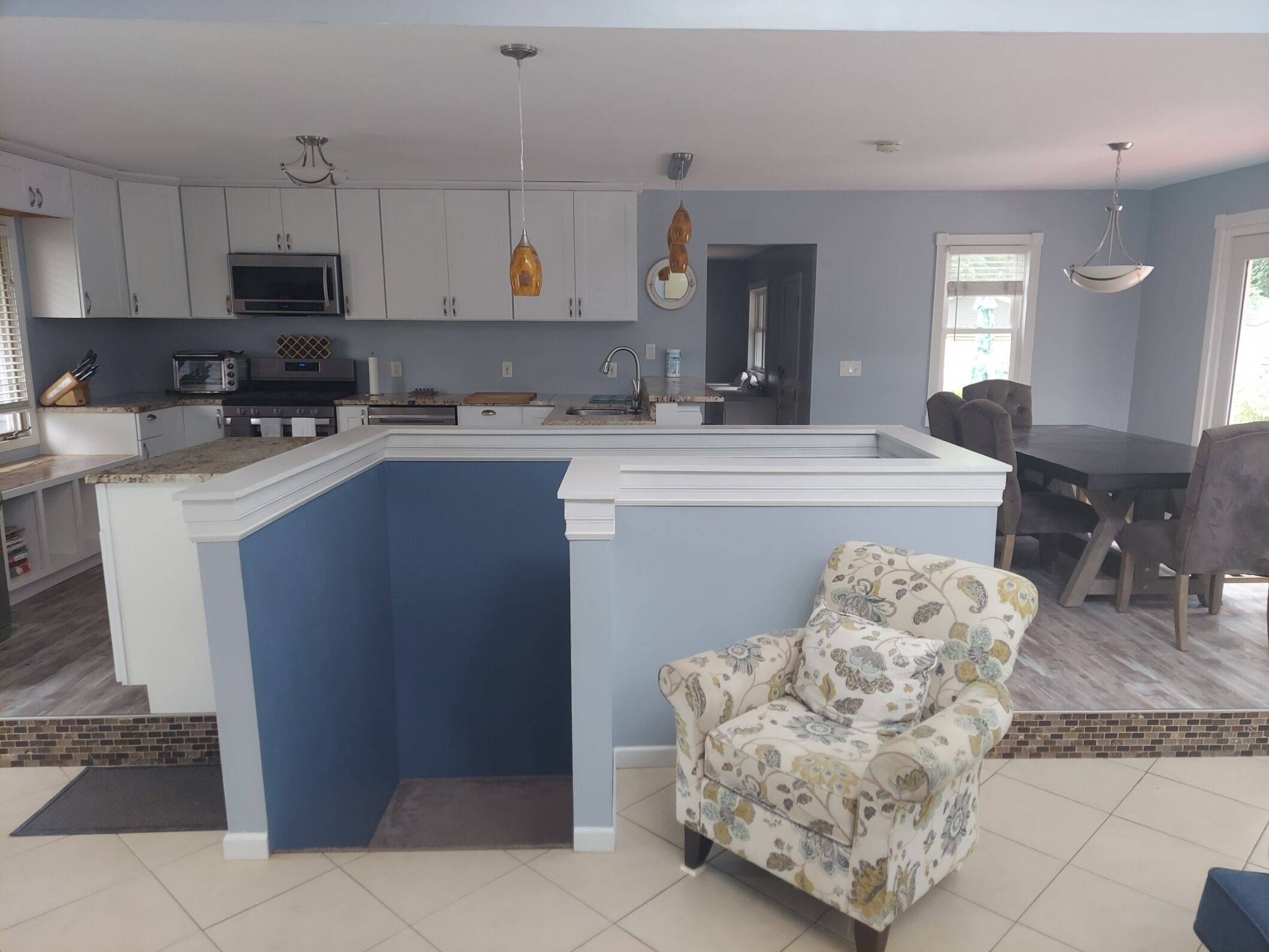 A modern kitchen with white cabinets, a blue accent wall, and a dining area with a table and chairs.