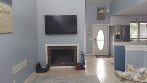 Ein Wohnzimmer mit Kamin, einem an der Wand befestigten Fernseher und einer Küchenzeile mit Kühlschrank.