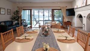Un comedor con una larga mesa dispuesta para seis personas, rodeada de sillas de madera, un jarrón grande con piedras decorativas y vistas a un lago a través de amplios ventanales.