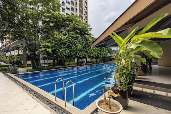 A swimming pool with clear blue water, surrounded by lush greenery and a modern building in the background.