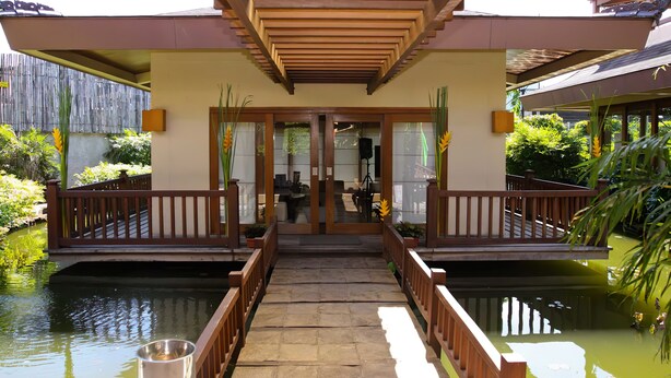A covered walkway leading to a building with a wooden railing and a pond on either side.