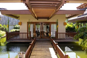 A covered walkway leading to a building with a wooden railing and a pond on either side.
