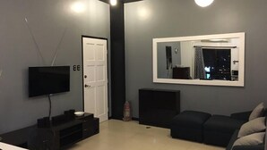 A modern living room with a flat-screen TV, a large mirror, and a dark-colored sofa.