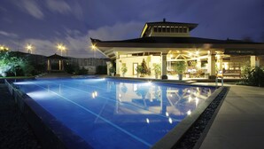 A swimming pool with a clear blue water surface, surrounded by a well-lit patio area with potted plants and outdoor seating.
