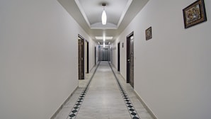 Un pasillo largo y estrecho con piso a cuadros, puertas a ambos lados y una lámpara colgante.
