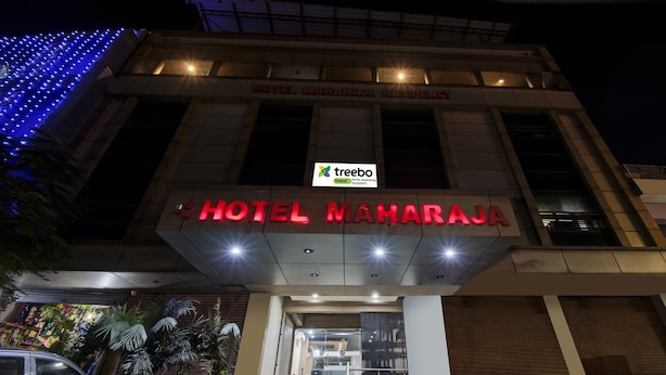 Exterior del Hotel Maharaja Residency, con señalización iluminada y fachada moderna.
