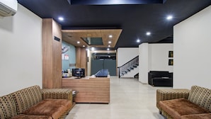 Un área de recepción moderna con un mostrador de madera, un monitor Samsung, un ventilador y una escalera que sube a un piso superior.