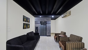 Una sala de estar moderna con un sofá negro, sillones estampados, una mesa de centro y un pasillo que conduce a un ascensor.