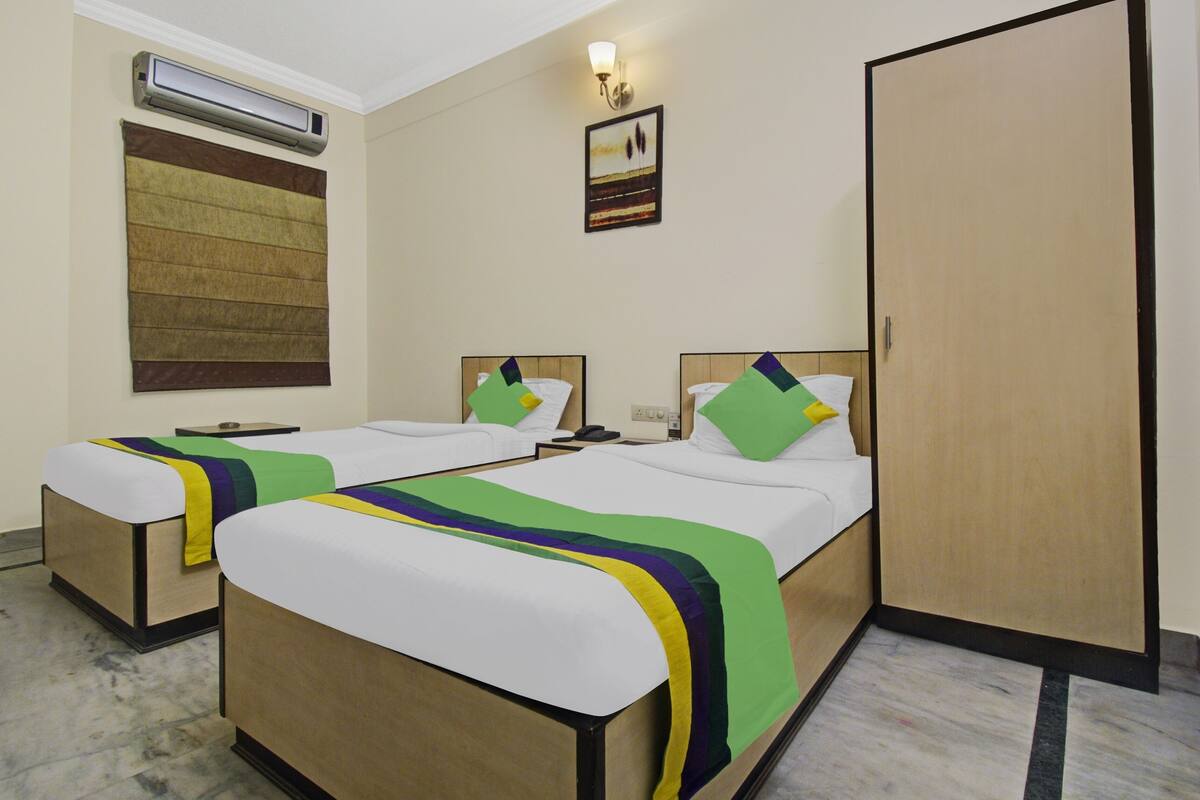 Habitación de hotel con dos camas individuales, un armario, aire acondicionado de pared, un cuadro y una lámpara.