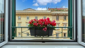 Finestra amb vistes a un edifici i un balcó amb una maceta de flors.