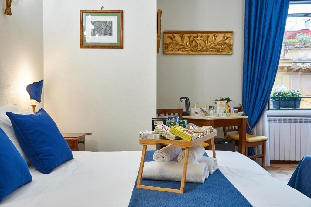 Une chambre d’hôtel avec un lit bien fait, une petite table avec des articles de toilette et une fenêtre ornée de rideaux bleus.
