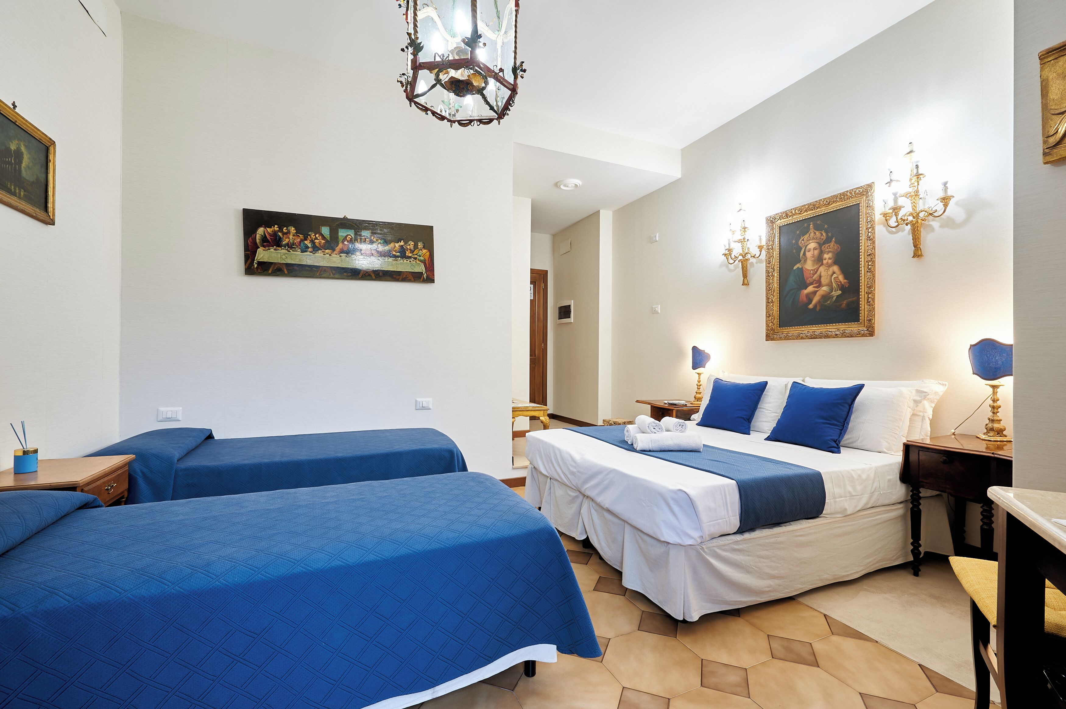 Ein Hotelzimmer mit zwei Einzelbetten, einem Doppelbett, einer Chandelier und Kunstwerken an den Wänden.