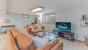 Ein Wohnzimmer mit einem braunen Ledersofa, einem Couchtisch, einem Fernseher, der Disney+ zeigt, und einem Bücherregal.