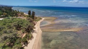 An aerial view of a beach with clear waters, a sandy shoreline, and surrounding vegetation.