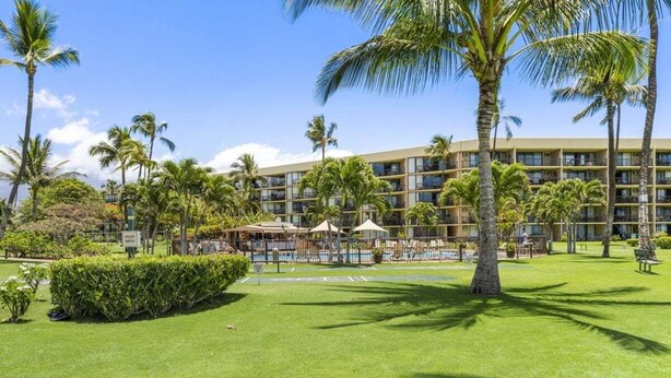 A hotel with a pool area, palm trees, and a well-maintained lawn.