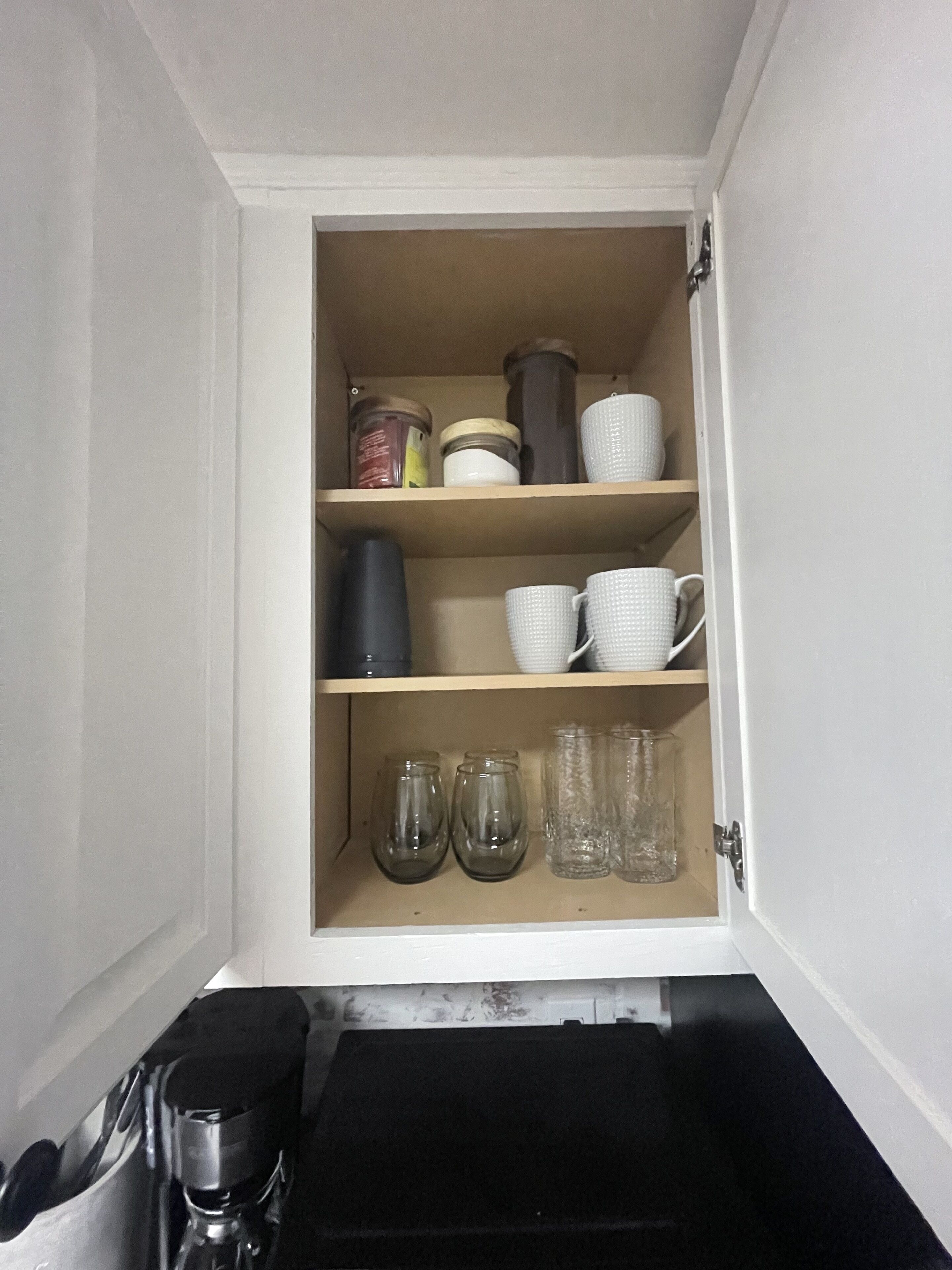 Un meuble de cuisine avec des étagères contenant des bocaux, des tasses et des verres.