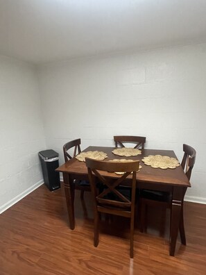 Un comedor con una mesa y sillas de madera, un cubo de basura y una pared blanca.