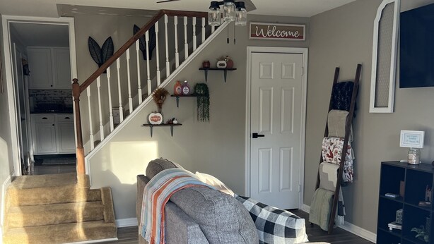 A living room with a grey sofa, a wooden staircase, a ceiling fan, and a 'Welcome' sign on the wall. - Cozy 1BR Apt Minutes From Skyline Drive!! (Amissville)