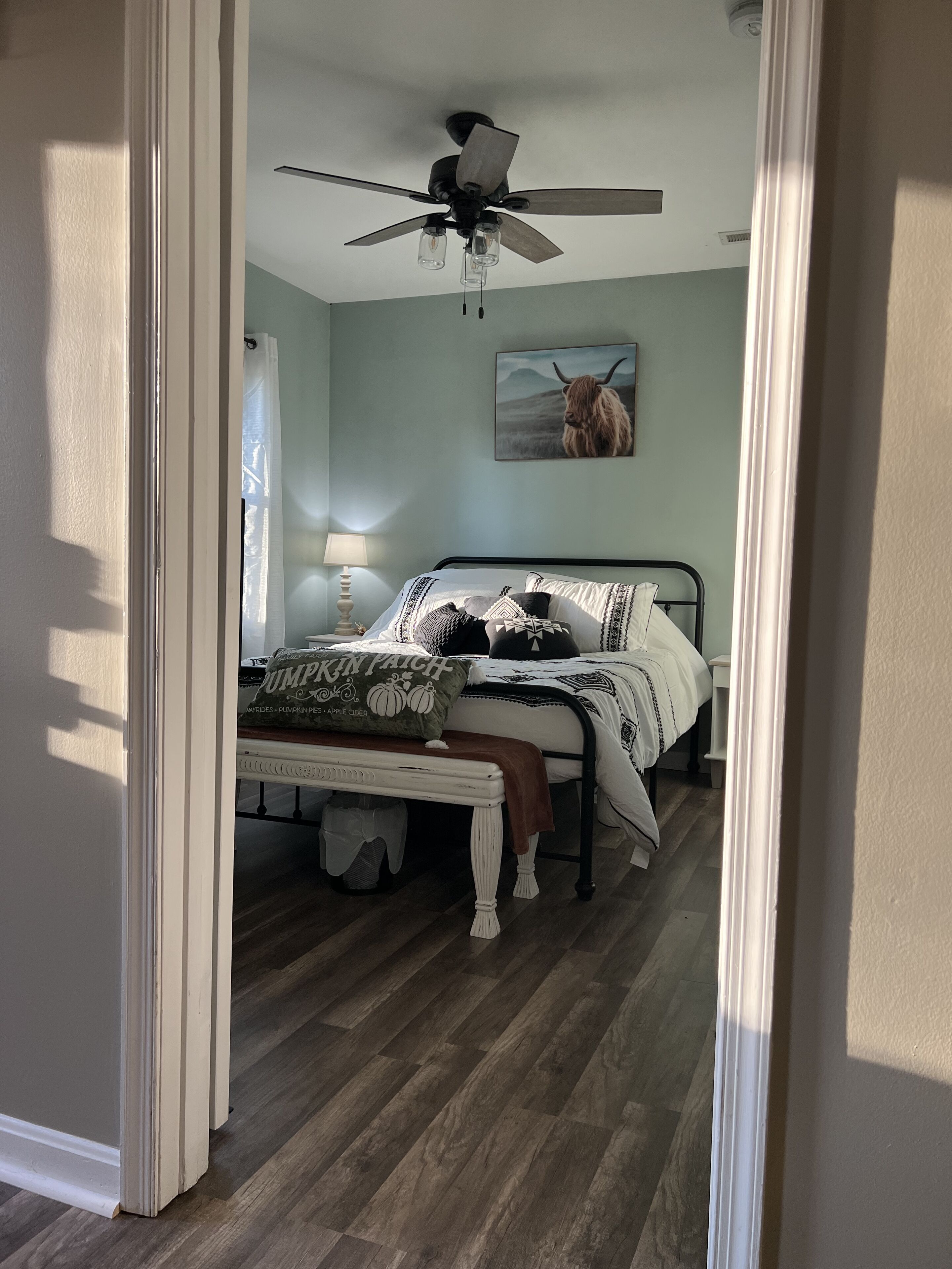 Ein Schlafzimmer mit einem Bett, einem Deckenventilator, einer Lampe und einem Gemälde einer Kuh.