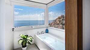 A bathroom with a bathtub, a potted plant, and a view of the sea and a hillside town. - Palazzo Vittoria with wonderful terrace & Jacuzzi (Campania)