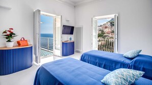 A hotel room with two beds, a TV, a potted plant, and a view of the sea and buildings. - Palazzo Vittoria with wonderful terrace & Jacuzzi (Campania)