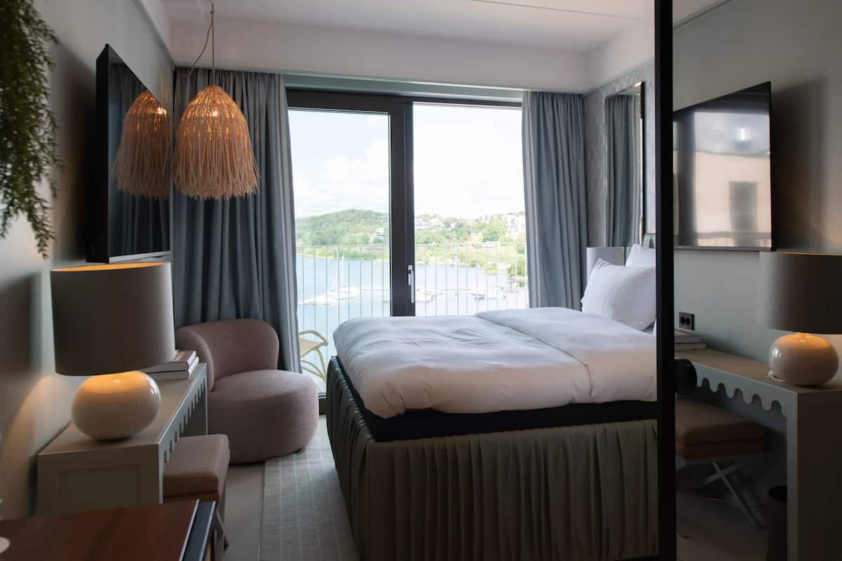 A hotel room with a bed, a desk, a chair, a TV, and a balcony with a view of the city.