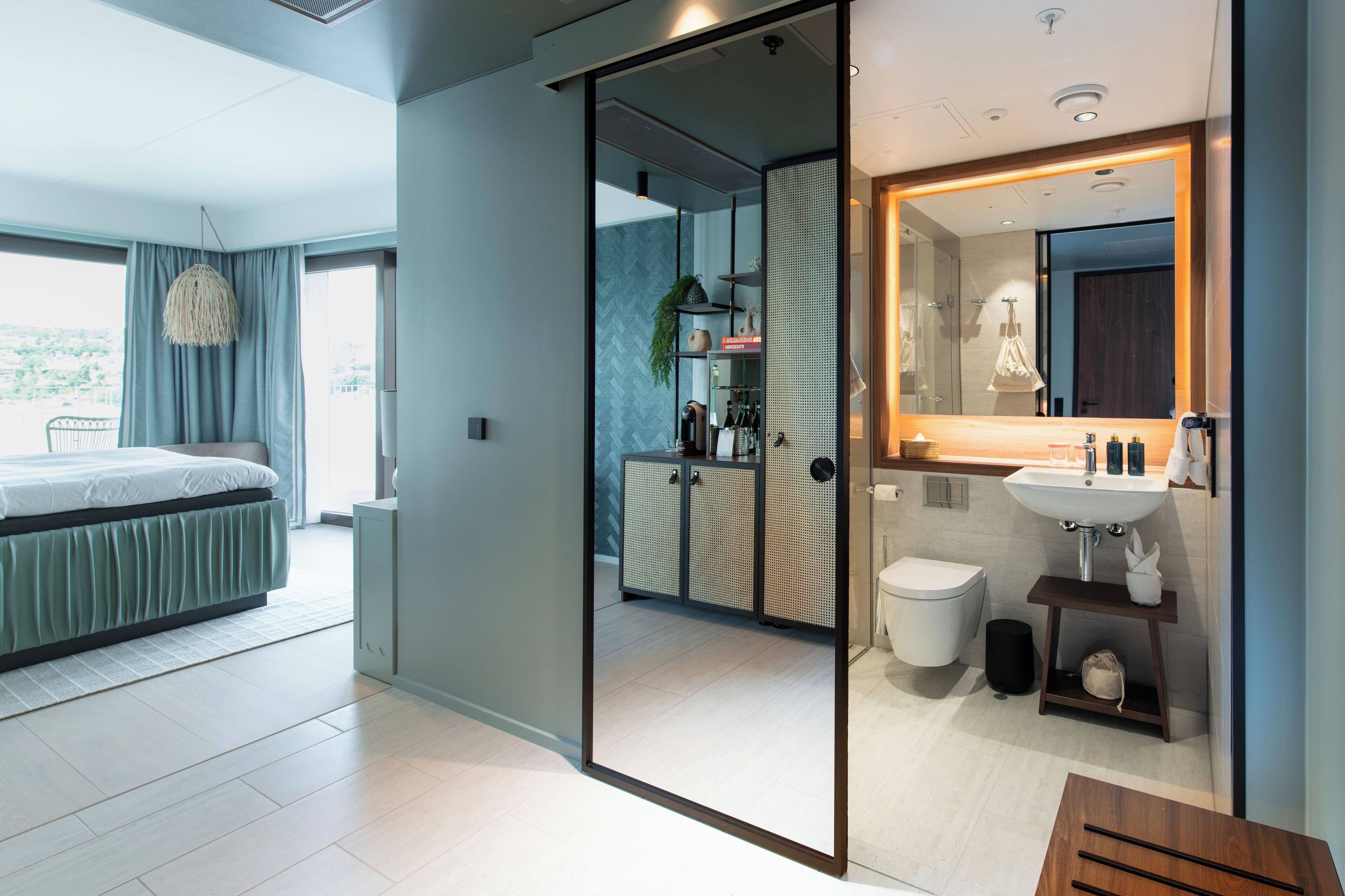 Habitación de hotel moderna con una cama grande, un baño con espejo y lavamanos, y vista a la ciudad.