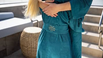 Una persona con una bata color turquesa con un logo en la parte delantera, de pie junto a un taburete tejido y unos escalones.
