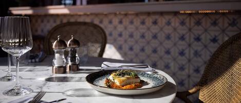 Una mesa de comedor con un plato de comida, saleros, pimenteros, un tenedor y una copa de vino.