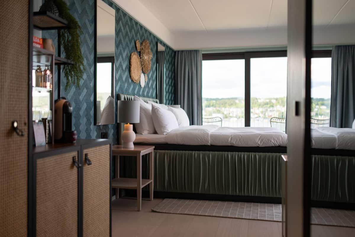 A bedroom with a bed, bedside table, and a view of the city through large windows.