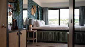 Una camera da letto con un letto, un comodino e vista sulla città attraverso ampie finestre.