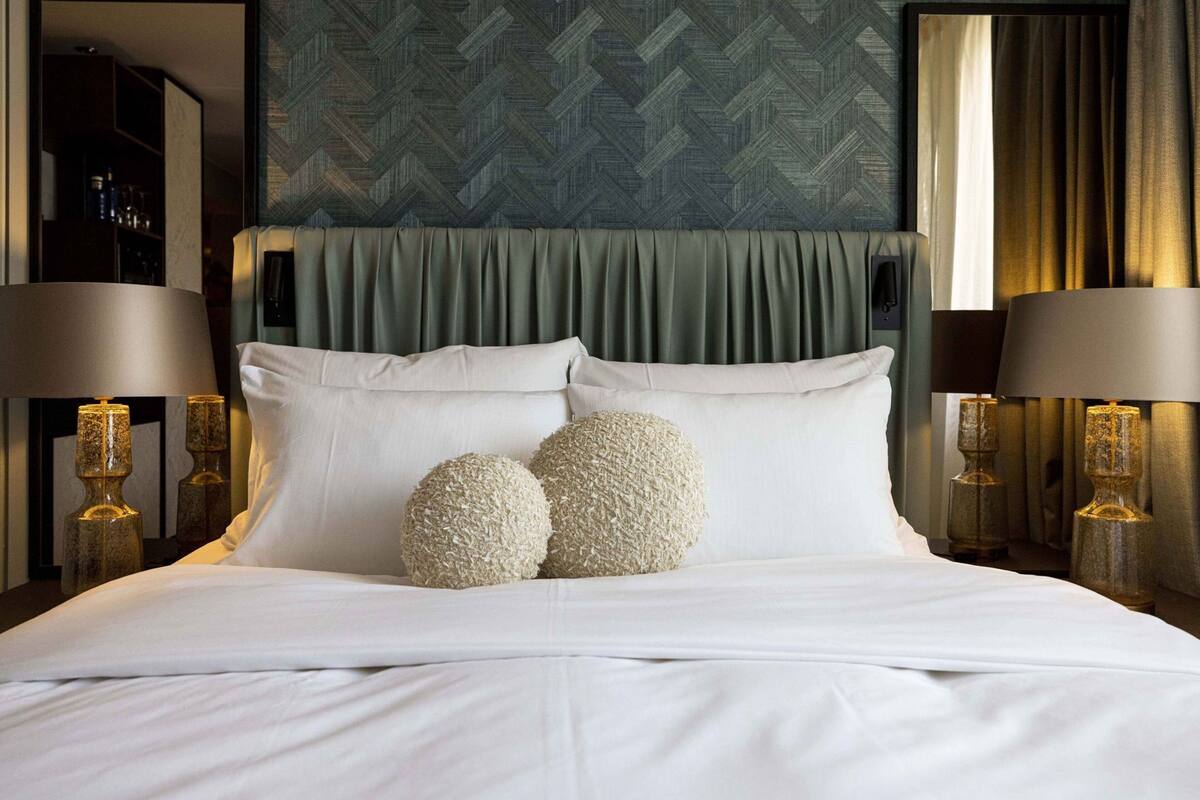 A neatly made bed with white linens, two round pillows, and a green patterned headboard.
