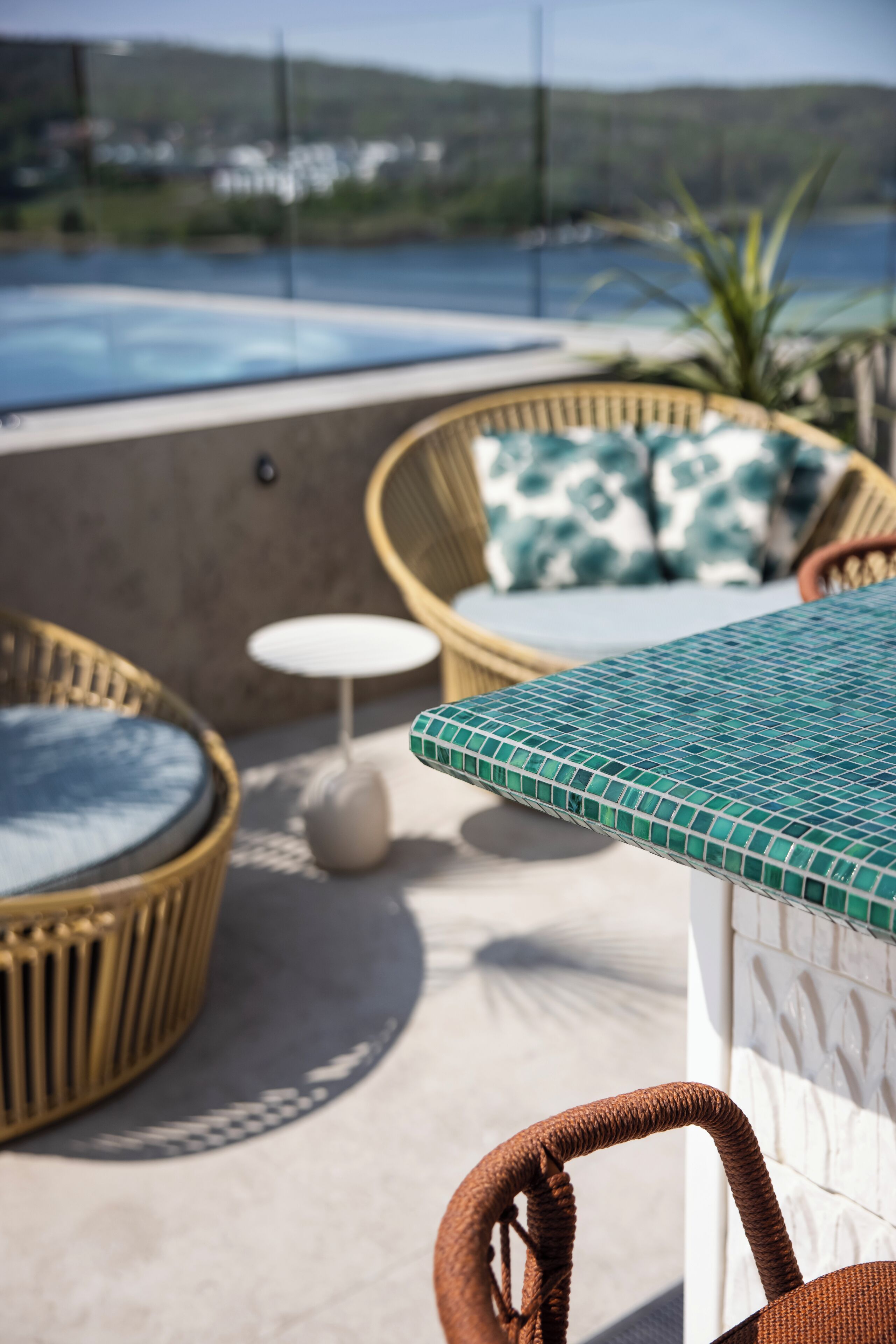 Un fauteuil de jardin en osier avec un coussin, une petite table ronde et un plateau de table recouvert de carreaux.