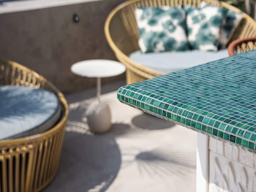 Una silla de mimbre con cojín, una mesita redonda y una superficie de mesa con azulejos.