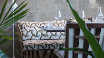 A dining area with a patterned sofa, a table set with glasses and a bottle, and a decorative hanging lamp.