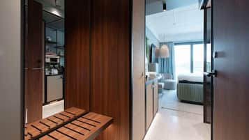 A modern hotel room with a wooden bench, a kitchenette, and a view of the city.