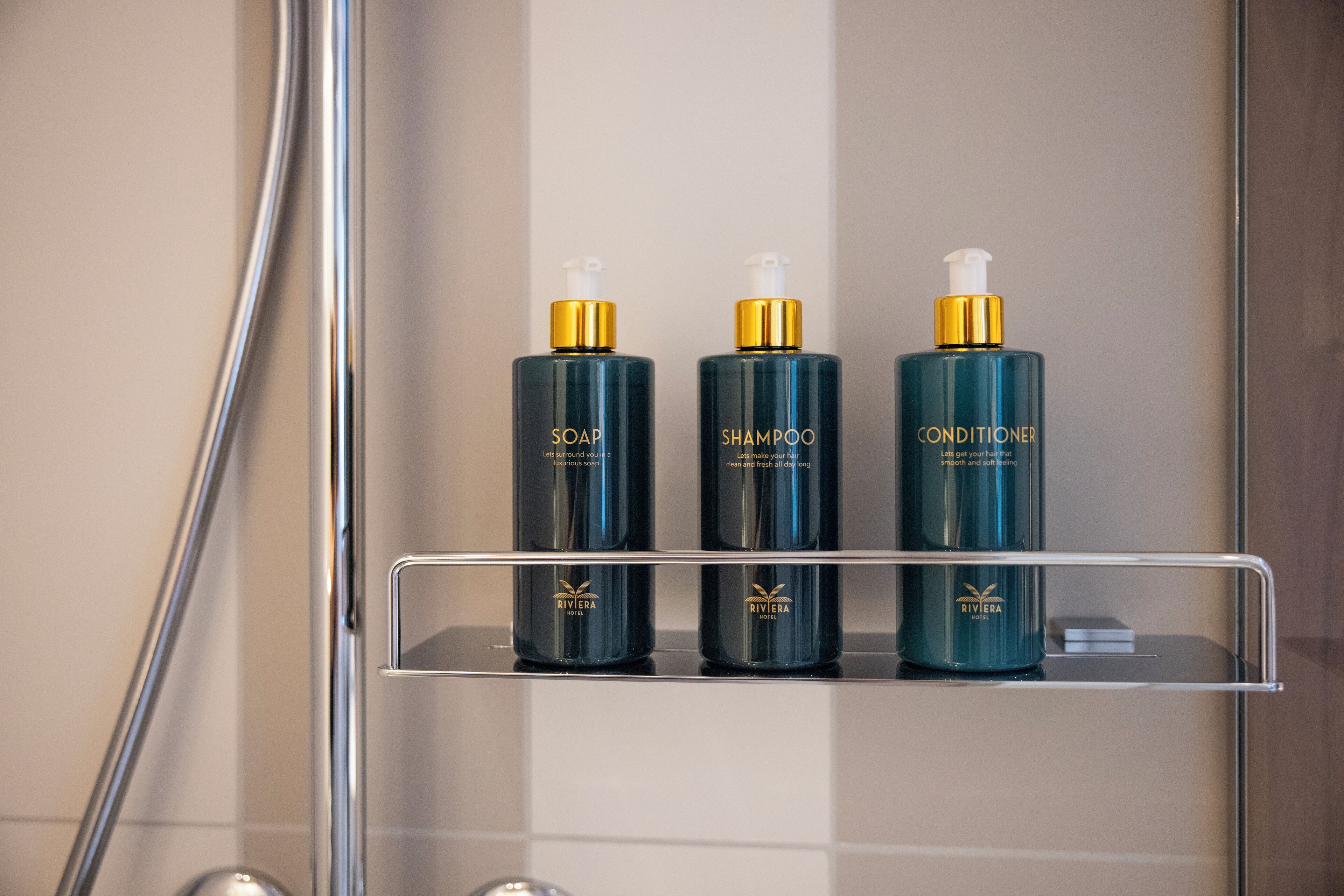Ein Badezimmerschrank mit drei Flaschen Rivera Hotel Toilettenartikeln: Seife, Shampoo und Conditioner.