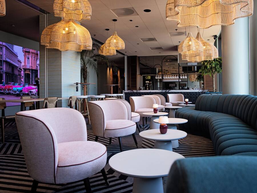 Un espacio lounge moderno con asientos cómodos, un bar y una pantalla grande que muestra un paisaje urbano.