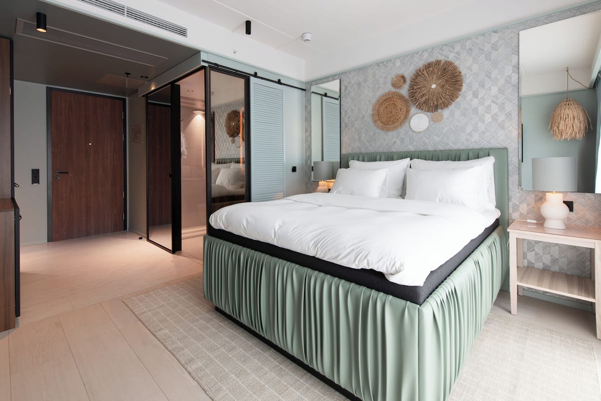 A modern bedroom with a large bed, a sliding door closet, a bedside table with a lamp, and a wall-mounted mirror.