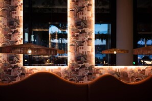 A restaurant interior with patterned wallpaper, hanging lamps, and a view of the cityscape through large windows.