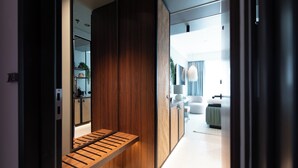 Un interior moderno con un banco de madera, un armario con espejo y una vista parcial de una sala de estar con sofá y lámpara.