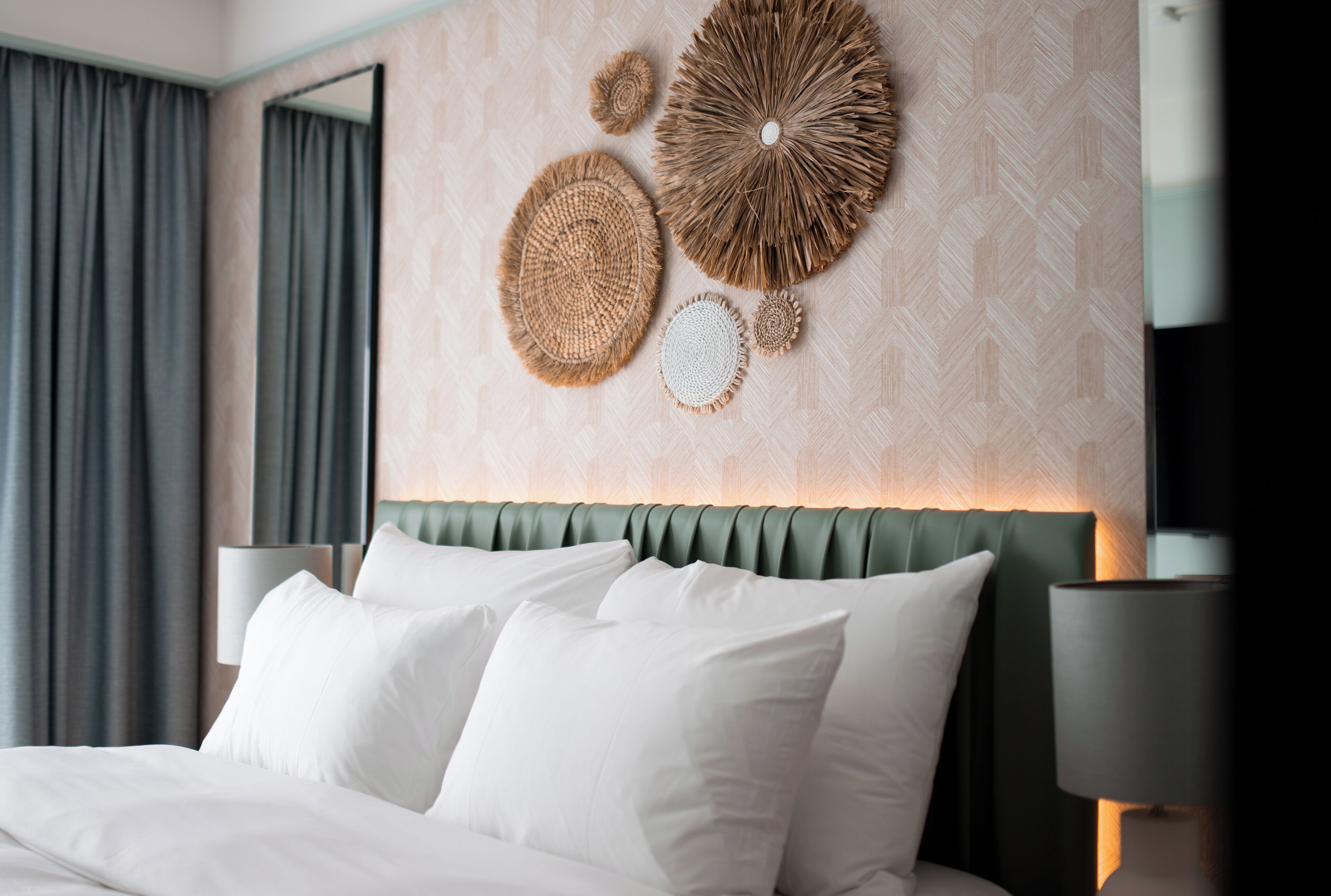 Una cama bien hecha con sábanas blancas, un cabecero tapizado en verde y decoración en la pared.