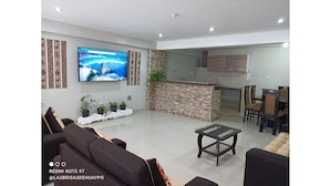 Ein modernes Wohnzimmer mit Flachbildfernseher, einer Couch, einem Couchtisch und einer Küchenzeile mit Steinrückwand.