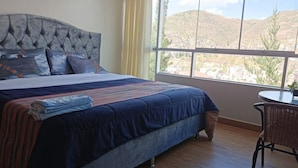 Ein Schlafzimmer mit einem großen Bett, einem Fenster mit Blick auf Hügel und einem kleinen Tisch mit Stuhl.