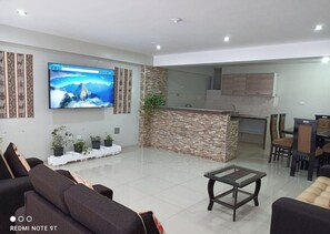 Ein modernes Wohnzimmer mit Flachbildfernseher, einer Couch, einem Couchtisch und einer Küchenzeile mit Steinrückwand.