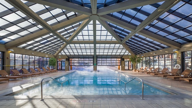 Piscina interior com teto de vidro, espreguiçadeiras e placa de 'Não Mergulhar'.